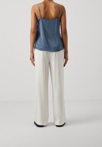 Camisole blu in satin con spalline regolabili, abbinato a pantaloni bianchi a gamba larga. Tessuto liscio, vestibilità rilassata e taglio alla caviglia.