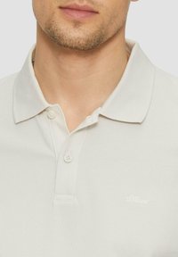 Lichtbeige polohemd van gestructureerde stof met een puntkraag en twee knopen. Bevat een klein, wit logo aan de linkerkant.