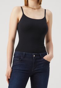 Top de tirantes finos ajustado negro, hecho de una tela suave. Combinado con unos jeans de mezclilla azul oscuro que tienen bolsillos frontales y un botón dorado.