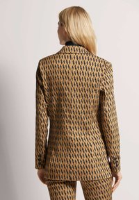 Bruine blazer met zwart abstract patroon, met een nauwsluitende pasvorm, met uitgesneden revers en twee knopen op elke manchett.