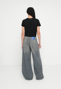 Fekete rövid ujjú póló és laza szabású szürke farmernadrág, kék logófolttal a derékon, hátulnézetből.