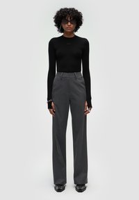 Czarna bluzka z długim rękawem, szare spodnie z wysokim stanem i szerokimi nogawkami, eleganckie czarne buty, srebrne akcesoria, gładka tekstura z minimalnym logo.