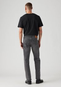 Vaqueros grises con un corte recto, que cuentan con una etiqueta de cuero en la parte trasera, dos bolsillos traseros y sutiles detalles de costura. Combinados con una camiseta negra.