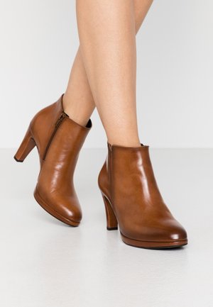 Bottes montantes en cuir marron avec une texture lisse, un bout arrondi et un talon haut. Elles disposent d'une fermeture éclair latérale.