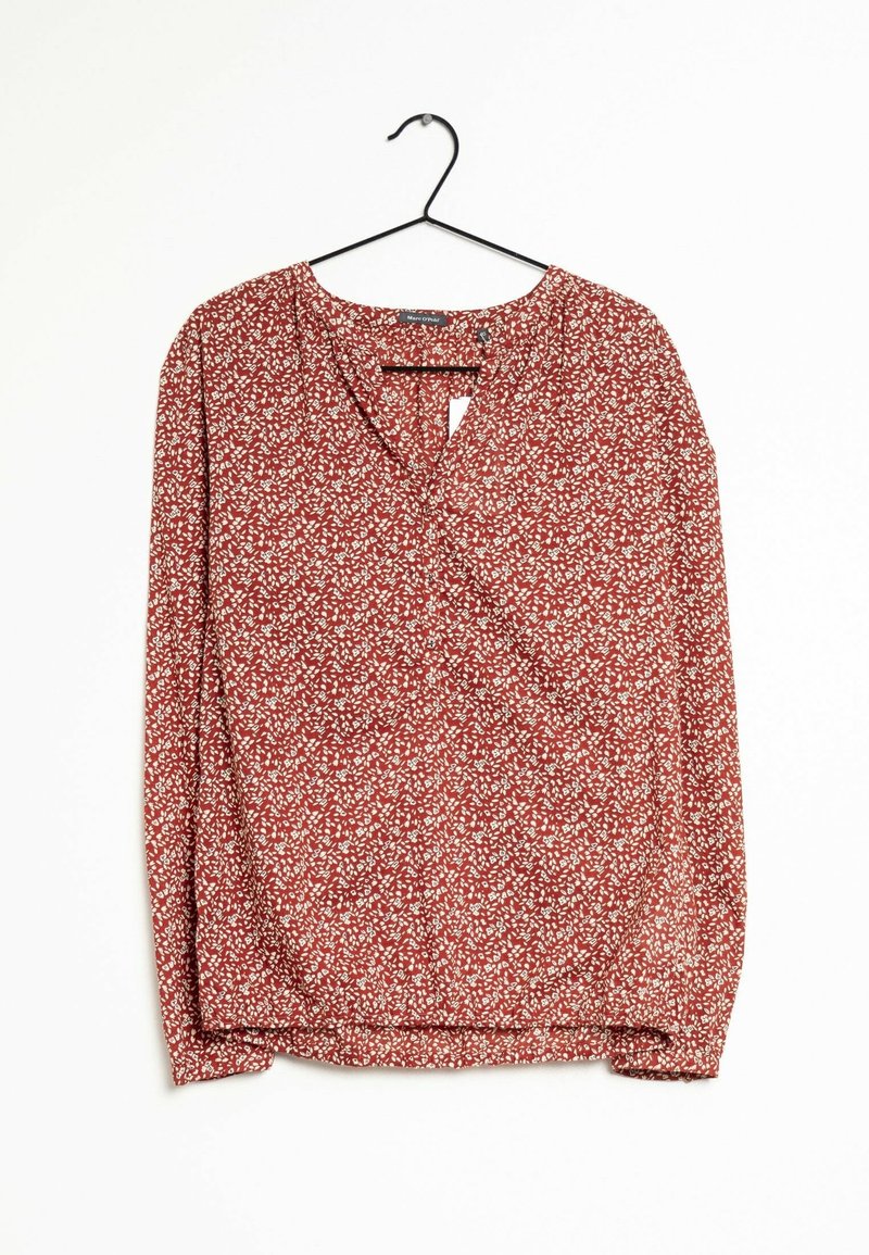 Blouse rouge à manches longues avec motif floral blanc suspendue sur un cintre noir sur fond blanc.