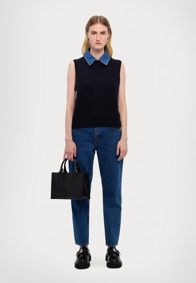Marineblauw mouwloos gebreid topje met een denim kraag, gecombineerd met blauwe rechtgesneden jeans, een zwarte leren handtas en zwarte chunky schoenen.