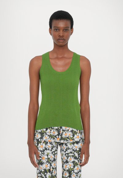 Débardeur vert côtelé avec un col rond, associé à un pantalon à motifs avec des marguerites blanches et des centres orange sur un fond sombre.