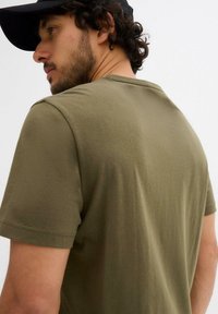 T-shirt a maniche corte color verde oliva, realizzato in tessuto morbido, con una texture liscia e una vestibilità rilassata, caratterizzato da dettagli di cucitura minimi.