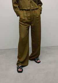 Khaki cropped jack met twee voorzakken, gecombineerd met wijde khaki broeken en zwarte sandalen met ronde hardware accenten.