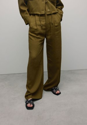 Khaki cropped jack met twee voorzakken, gecombineerd met wijde khaki broeken en zwarte sandalen met ronde hardware accenten.