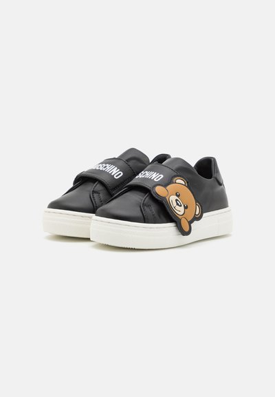 Sneakers in pelle nera con cinturino in Velcro e testo bianco "Moschino" insieme a un logo con orso marrone. Suola in gomma con dettagli testurizzati.