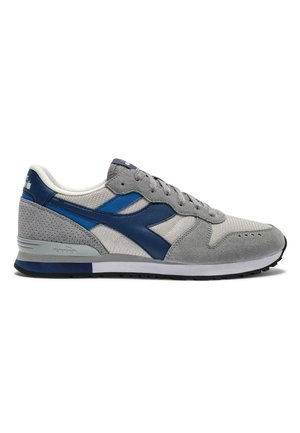 Scarpa da ginnastica atletica grigia e blu con tomaia in camoscio e mesh, chiusura con lacci e suola in gomma con motivo, mostrata di lato su sfondo bianco.