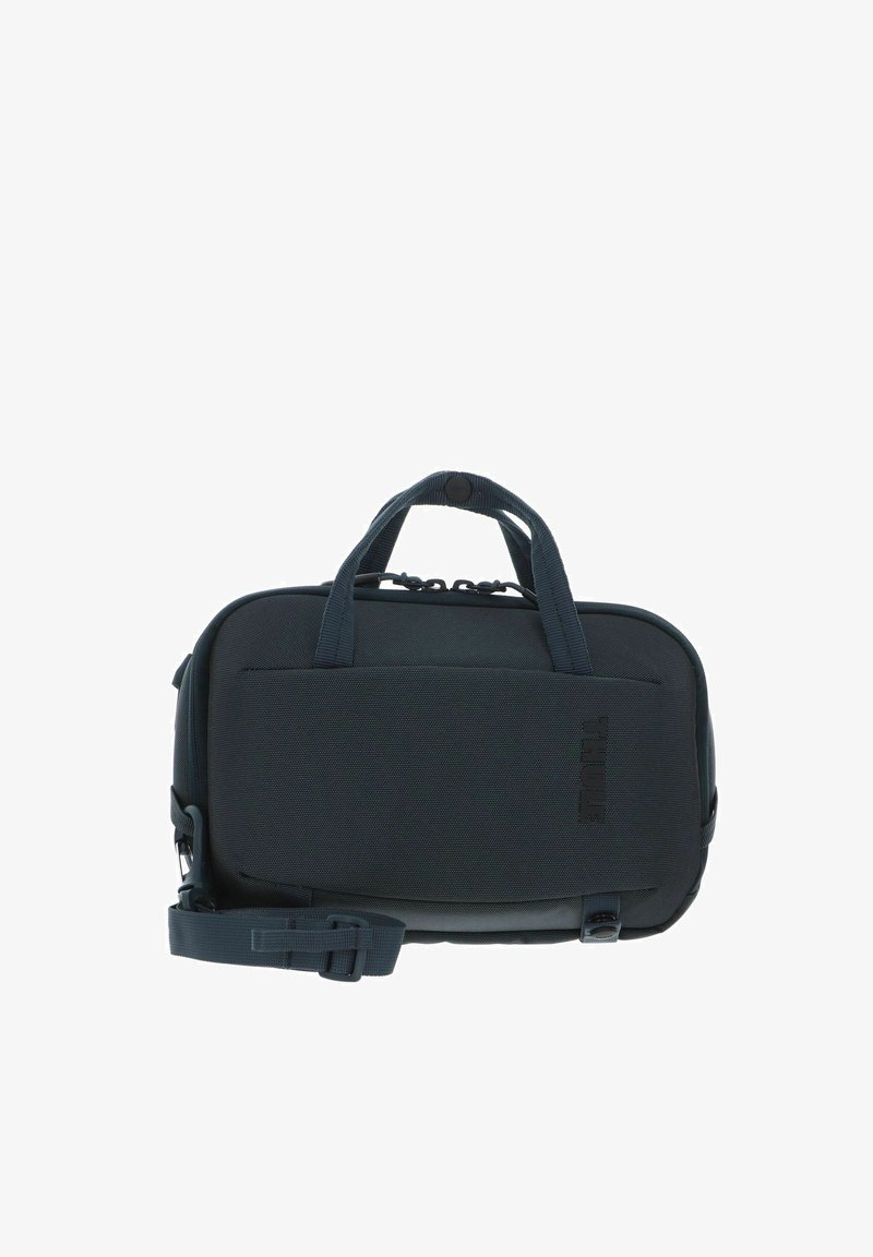 Sac de transport Thule compact de couleur gris foncé avec double poignées, poche avant et bandoulière réglable.