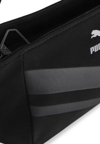 Čierna látková taška s hladkým povrchom, s šedými vodorovnými pruhmi a výrazným strieborným logom Puma. Obsahuje zips a kovové doplnky.
