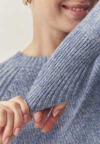 Pull bleu clair en maille avec texture côtelée et manches légèrement oversize, présentant un matériau doux et une coupe décontractée.