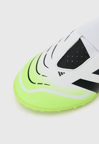 Zapatilla deportiva blanca y negra con una suela verde neón. Presenta un upper liso y acentos texturizados, con líneas y patrones curvos distintivos.