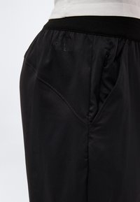 Nahaufnahme von schwarzen North Face-Hosen mit geripptem Bund, seitlicher Reißverschlusstasche und abgesteppten Paneel-Details in Hüfthöhe.