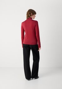 Červená dlhá rukávová roláková košeľa so slim fit strihom, skombinovaná s čiernymi nohavicami s vysokým pásom, ktoré majú jemné trblietky a rovný strih.