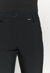 Schwarze Hose aus einem glatten, dehnbaren Stoff mit vorderen Taschen, einem sicheren Knopfverschluss und einem seitlichen Reißverschlussdetail.