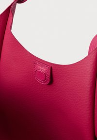 Różowa torba na ramię ze skóry o gładkiej fakturze. Posiada zaokrąglony pasek na ramię oraz okrągły zatrzask jako zapięcie.