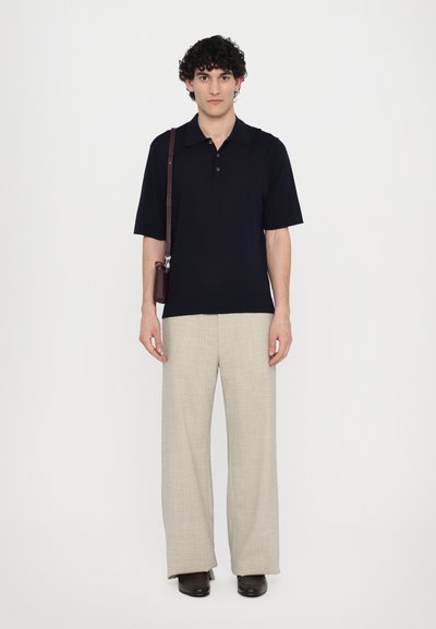 Polo à manches courtes bleu marine, pantalon large beige et chaussures foncées ; style moderne et minimaliste avec une palette de couleurs polyvalente.
