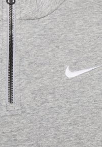 Šedá mikina na zip z měkké tkaniny s kontrastním černým zipem a malým bílým logem Nike na levé straně hrudi.