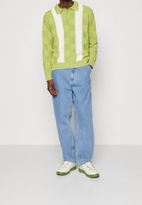 Groene gebreide polo met witte verticale strepen, gecombineerd met lichtblauwe wijde denim jeans en witte sneakers met groene accenten.