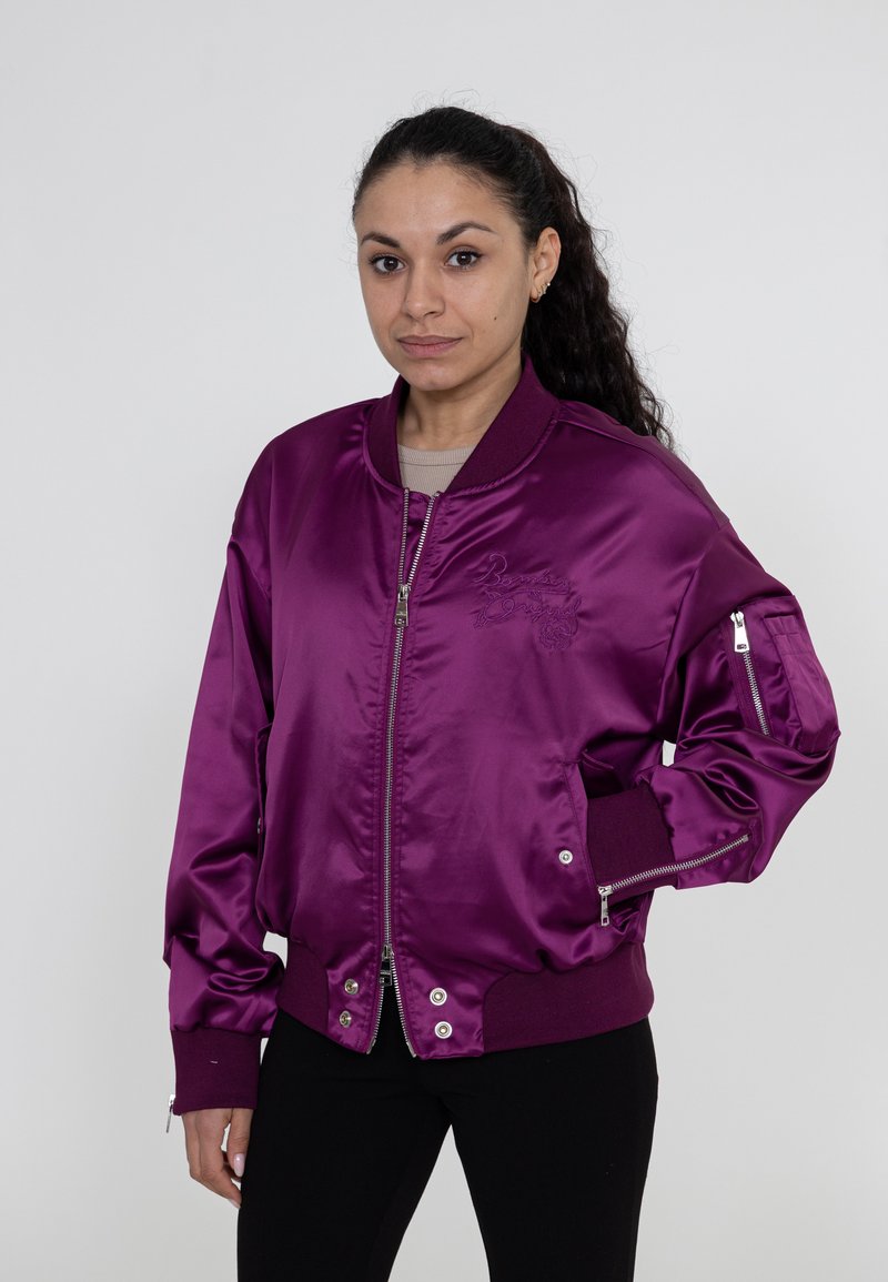 Satijnen bomberjack in diep paars met geribbelde manchetten. Voorzien van zijzakken, een ritsluiting aan de voorkant en een klein geborduurd logo op de borst.