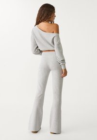 Šedá zkrácená mikina s off-shoulder designem, spárovaná s odpovídajícími šedými rozšířenými tepláky, obojí vyrobené z jemné texturované látky.