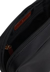 Black nylon pouch featuring a zip closure, textured interior, and a brown leather label inside. Accented with gold hardware.