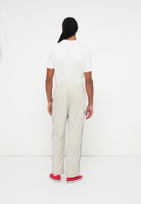 Jasnoszare dresy z czarnymi wstawkami po bokach, w połączeniu z białą koszulką z krótkim rękawem i czerwonymi trampkami, widok z tyłu.