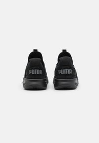 Scarpe da ginnastica nere con una tomaia testurizzata, collare imbottito e un evidente marchio PUMA sul tallone. Suola in gomma liscia per la trazione.