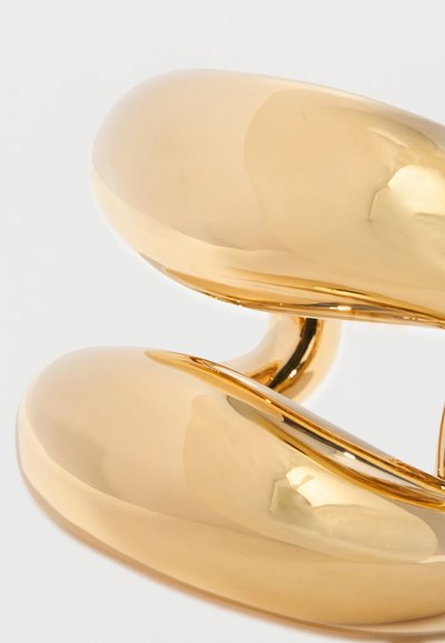 Zwei glänzende, glatte, gebogene goldene Metallobjekte, eng übereinander gestapelt auf einem schlichten weißen Hintergrund.