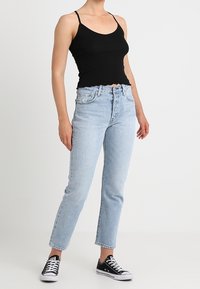 Černý žebrovaný tank top s tenkými ramínky, kombinovaný se světle modrými džíny s vysokým pasem a rovnými nohavicemi a černými plátěnými teniskami.