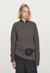 Tekstil grå kabelstrikket sweater med rund hals, lagd over en mørk skjorte, parret med mørke bukser og en brun bæltepose.