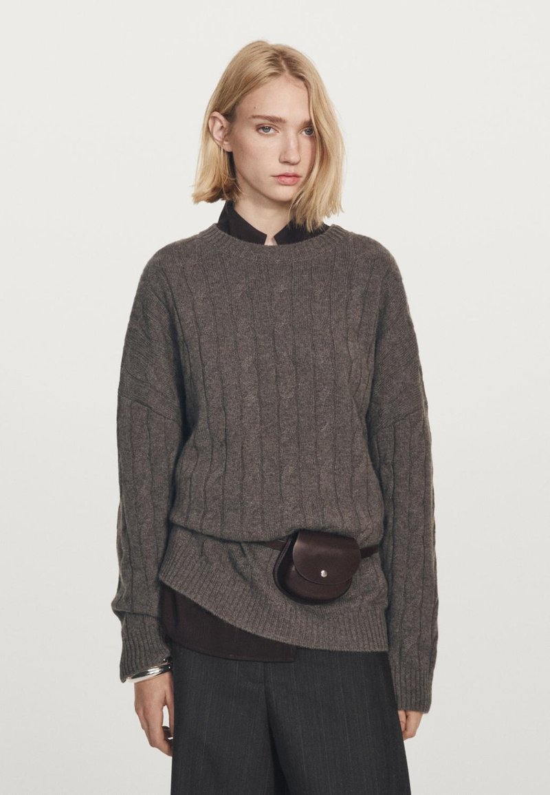 Tekstil grå kabelstrikket sweater med rund hals, lagd over en mørk skjorte, parret med mørke bukser og en brun bæltepose.