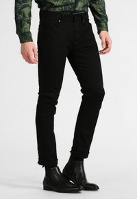 Black slim-fit jeans, made from denim, with a smooth texture, front pockets, and side seams. Worn with black ankle boots.