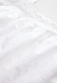 Tessuto di cotone bianco con delicato ricamo floreale e dettagli texturizzati al collo. Morbido, leggero e leggermente trasparente.