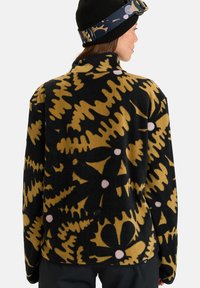 Pullover in fleece con base nera, caratterizzato da un audace motivo floreale senape, colletto alto e trama morbida. Adatto per l'uso all'aperto.