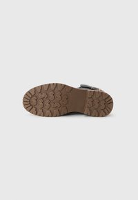 Semelle en caoutchouc marron avec un motif de semelle profonde sur une botte d'hiver noire avec doublure en fourrure, présentée sur un fond blanc.