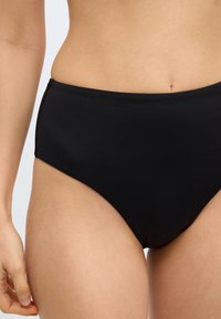 Μαύρο μαγιό σε σλιπ ψηλόμεσο, φτιαγμένο από λείο, ελαστικό ύφα σμα με καθαρό, απλό σχέδιο χωρίς ορατά στοιχεία ή μοτίβα.