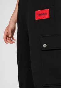 Zwarte sweatpants met een rood geborduurd "HUGO" label en een zijzak met een zilveren knoopdetails. Zacht materiaal met een slank ontwerp.