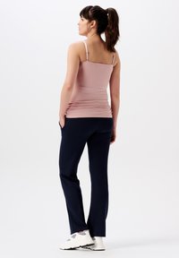 Ljusrosa tajt linne med smala axelremmar, kombinerat med marinblå byxor och vita träningsskor. Slät textur, strömlinjeformat design.