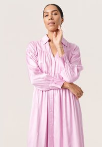 Abito rosa bottonato realizzato in tessuto lucido, con un corsetto aderente, dettagli arricciati e maniche lunghe con polsini.