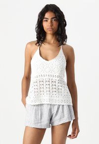 Hvit heklet tanktop med blomstermønster, med V-hals og spaghettistropper, kombinert med grå og hvite stripete shorts.
