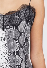Svart och vit ärmlös topp med spetskant som har ett ormskinnsmönster, framhäver subtila texturer och mönster genom hela designen.