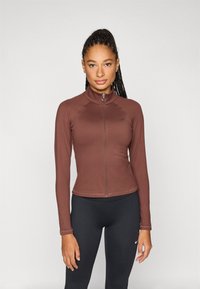 Καφέ μπουφάν με φερμουάρ και ψεύτικο γιακά, εφαρμοστό σχέδιο, μακριά μανίκια και λεία υφή. Διαθέτει ραφές σε τόνο και διακριτικό λογότυπο.