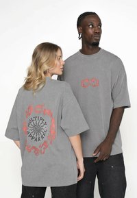 Szare, oversize'owe t-shirty wykonane z miękkiego materiału, z czerwonymi grafikami na plecach i przodzie, z krótkimi rękawami i luźnym krojem.