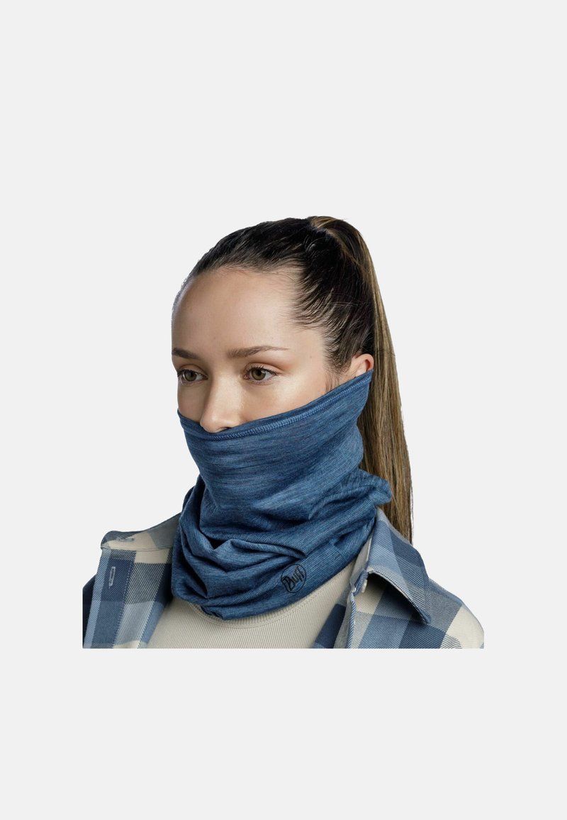 Gaiter blu in tessuto morbido ed elastico con una consistenza liscia. Presenta un dettaglio del logo ed è indossato sopra una camicia a quadri.