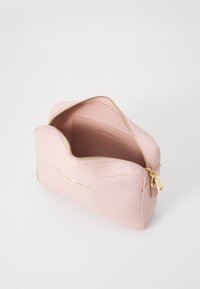 Borsa cosmetica in pelle rosa con cerniera e hardware dorati, caratterizzata da una superficie liscia e da un marchio in rilievo sulla parte anteriore. Vista dall'alto aperta.